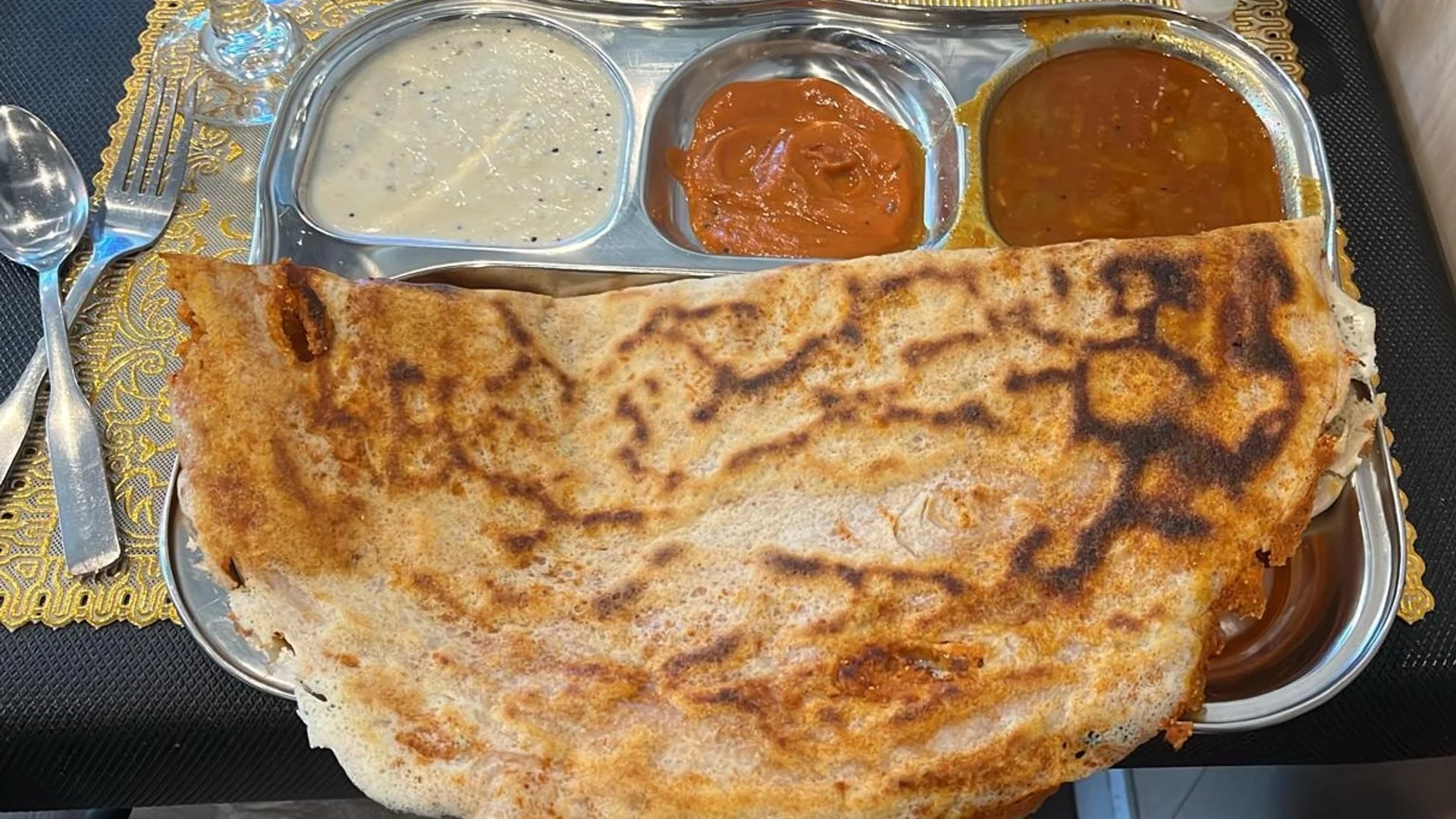 A thali plate with a crispy, full-size mysore masala dosa served with 3 sides of dipping options including a coconut chutney, tomato chutney, and sambar at Spice Grill in Jacksonville, Florida.